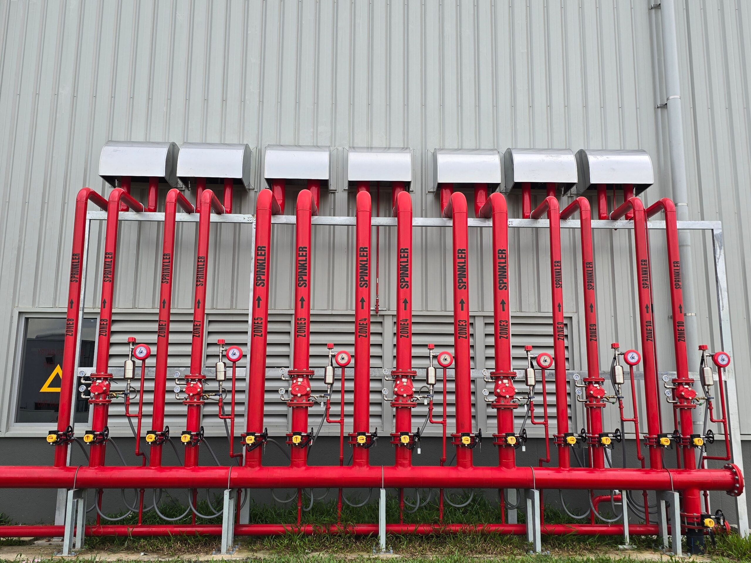 Home Red industrial fire sprinkler pipes aligned on a factory exterior wall.